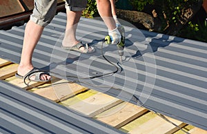 Roofing Construction. Roofer with crew gun installing  lightweight metal roof tiles roofing  construction on house roofing
