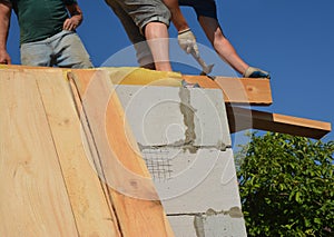 Roofing construction. The roofers are installing a wooden roof beam, roof truss on a concrete block house