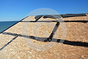 Roofing construction and waterproofing. A close-up of OSB roof deck, roof sheathing with hot rubberized asphalt, bitumen, tar