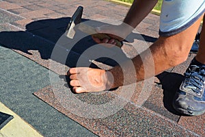 Roofing contractor installing roof tiles, asphalt shingles with hammer and nails. Roofing construction