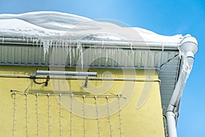 The roofs of the buildings are covered with snow and ice after a big snowfall. Huge icicles hang from the facades of buildings and