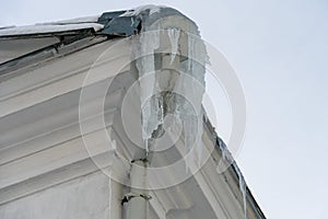 The roofs of the buildings are covered with snow and ice after a big snowfall. Huge icicles hang from the facades of buildings and