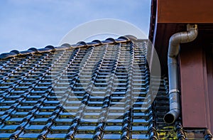 Rooftop with black glossy roof tiling and a drainpipe, modern dutch architecture background