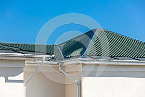 Rooftop of house with metal rain gutter system against blue sky