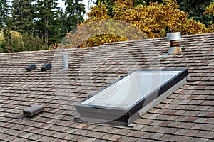 Rooftop view of residential asphalt shingle roof, skylight, roof vents, fall foliage in background