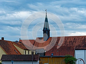 Rooftops of old German village with stork high up on cross of church spire against cloudy blue sky