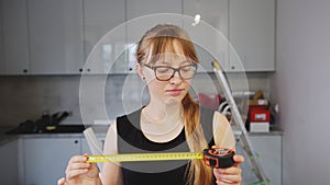 Rookie blue collar worker woman looking at a tape measure. Young female creator using a tape measure. Indoor shot.