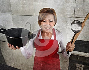 Rookie home cook woman in red apron at home kitchen holding cooking pan and rolling pin crying sad in stress