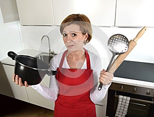 Rookie home cook woman in red apron at home kitchen holding cooking pan and rolling pin sad in stress confused and helpless