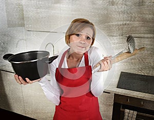 Rookie home cook woman in red apron at home kitchen holding cooking pan and rolling pin sad in stress confused and helpless