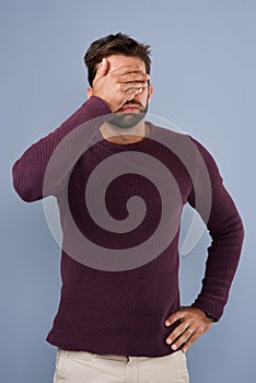 Rookie mistake. Studio shot of a young man covering his eyes in regret against a gray background.