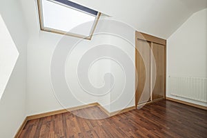 A room on the attic floor with skylights with blinds and a built-in wardrobe with sliding wooden doors and dark laminated flooring