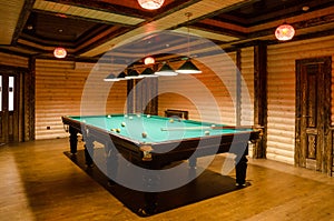 Room billiards decorated in dark wood with low lamps, billiard table with green cloth