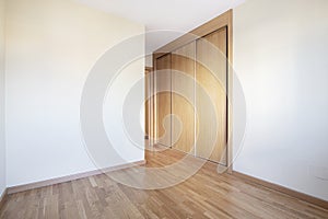 Room with a built-in wardrobe with three sliding oak doors with matching skirting boards and floors and smooth white walls