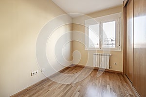 Room with a built-in wardrobe with three sliding oak doors with skirting boards and matching floors and smooth cream-colored walls