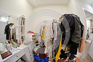 A room cluttered with clothes and a female dressing table with cosmetics, no closet