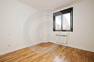 Room of an empty house with glossy oak parquet floors with black anodized aluminum window and white aluminum radiator under the