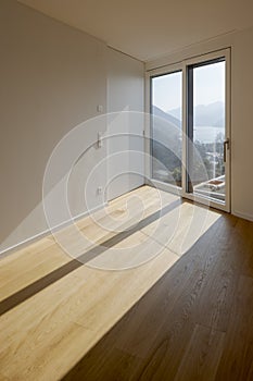 The room has white walls and wooden floors. Sunlight streams through the window