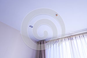 Room in house, with white curtains, fire sprinklers and LED light bulbs on white ceilings