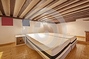 Room in a mezzanine with ceilings with wooden beams and mattresses without bedding