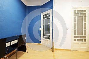 A room with old solid wood doors with translucent windows, blue and white walls and a black desk with white drawers