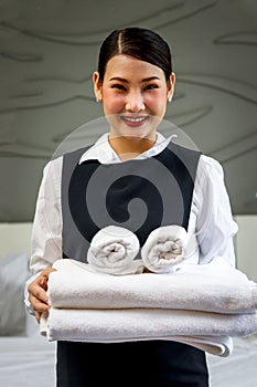Room service maid cleaning and making bed hotel room concept, portrait of young beautiful Asian smiling female chambermaid holding