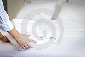Room service maid cleaning and making bed hotel room concept, woman hands putting stack of fresh white bath towels on bed sheet