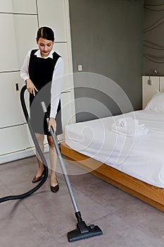 Room service maid cleaning and making bed hotel room concept, young beautiful Asian female chambermaid vacuuming the floor at