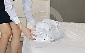 Room service putting stack of fresh white bath towels on the bed sheet. Female housekeeper putting clean towels on bed. Room