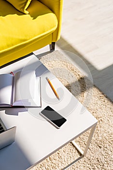 Room with sofa and table with laptop, smartphone and notepad in sunlight