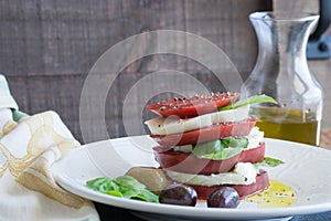 Closeup Caprese Salad with sliced red tomato, buffalo mozzarella, basil leaves and healthy whole olives dripping in extra virgin o