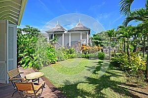 Room view of an open air porch with slightly extended roof and tall full length wooden door overlooking beautiful green garden