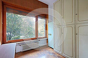 Room with wardrobe and large window, apartment interior in old house with garden