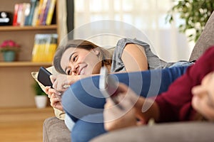 Roommates using their smart phones lying on a couch photo