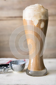 Root beer float in a tall pilsner glass, with vanilla ice cream melting, shown with thumb press disher.
