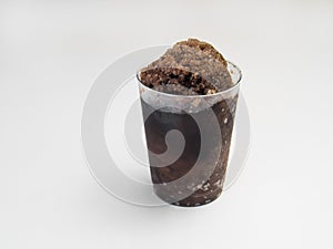 Root beer Hawaiian Shave ice, Shaved ice or snow cone in a clear plastic cup against a white background.