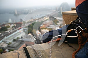 Rope access abseiler sitting over high rise building edge having hardware descender device clipping on 10.5 mm Dynamic low stretch photo