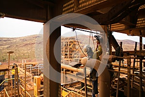 Rope access technician abseiling with twin ropes working at height commencing electric magnet drilling into the metal structure photo