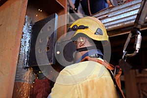 Rope access welder wearing helmet safety harness fall protection using ear plug noise protection while grinding weld plate