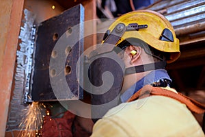 Rope access welder wearing safety helmet fall protection using ear plug noise protection while grinding weld plate