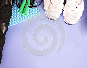 Rope, bottle for water, dumbbells and sports shoes on a blue background.Top view with copy space.