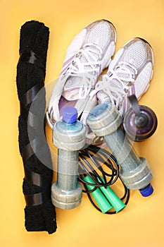 Rope, bottle for water, dumbbells and sports shoes on a yellow background.Top view with copy space.