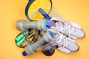 Rope, bottle for water, dumbbells and sports shoes on a yellow background.Top view with copy space.