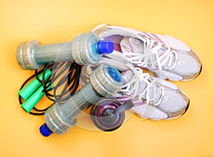 Rope, bottle for water, dumbbells and sports shoes on a yellow background.Top view with copy space.