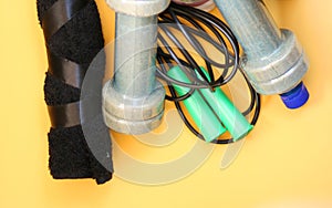 Rope, bottle for water, dumbbells and sports shoes on a yellow background.Top view with copy space.