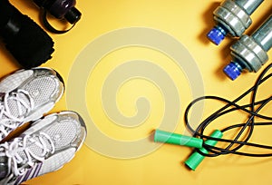 Rope, bottle for water, dumbbells and sports shoes on a yellow background.Top view with copy space.