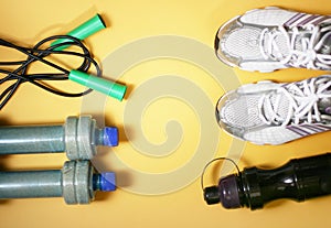 Rope, bottle for water, dumbbells and sports shoes on a yellow background.Top view with copy space.