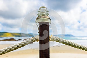 Rope fence on wooden pillar with glass lamp on beach.