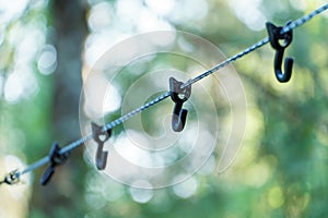 A rope with hooks for drying clothes during a hike is stretched between the trees in the forest. A tourist camp in the wild. Hooks