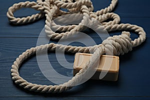 Rope noose and soap bar on blue wooden table, closeup